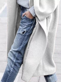 Person wearing a long coat over a sweater and jeans on a light background