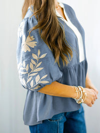 Person wearing a blue blouse with white floral embroidery on a plain background