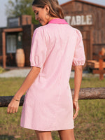 Woman wearing a pink and white striped dress standing outdoors with a wooden building in the background.