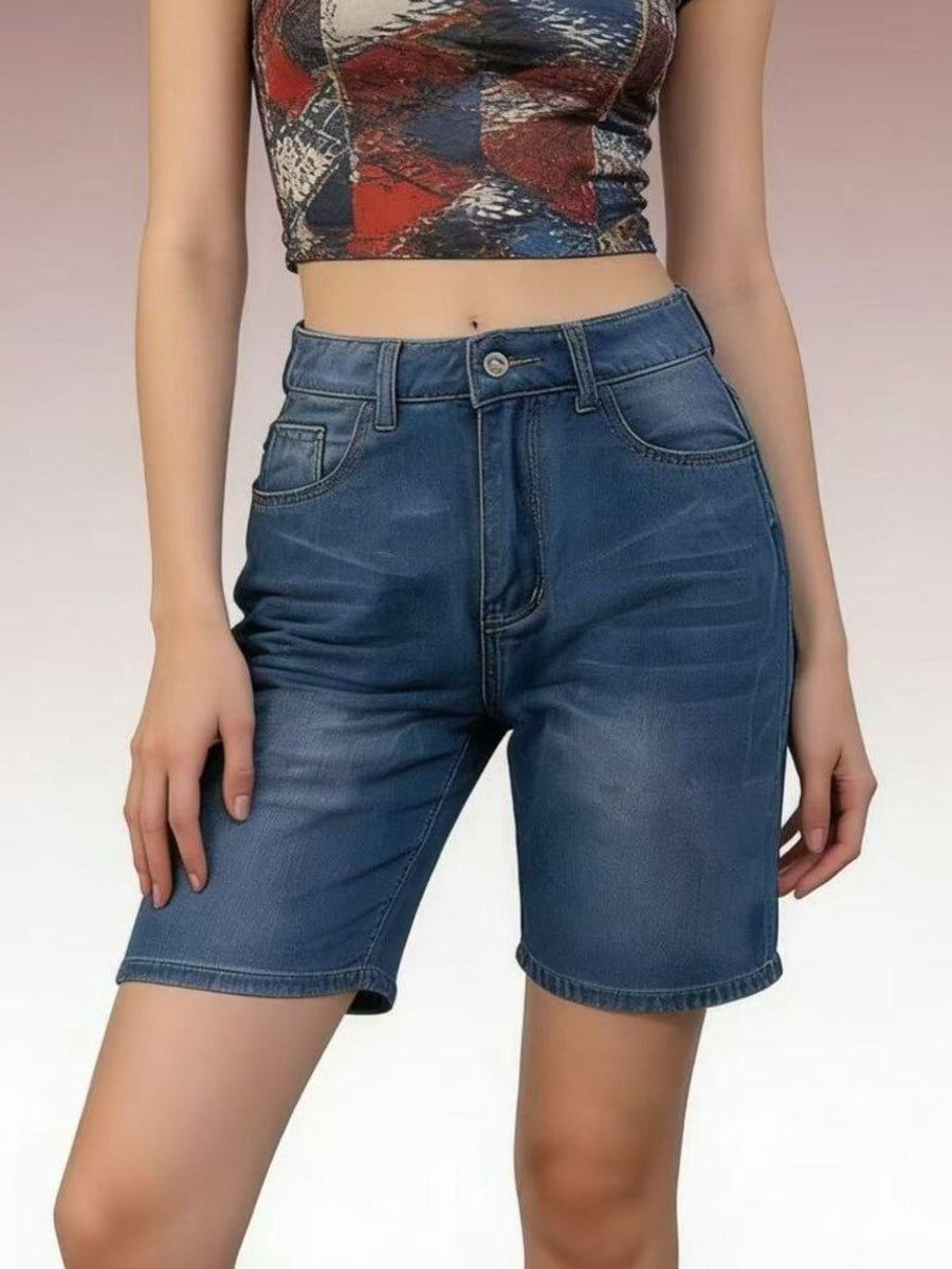 Person wearing blue denim shorts and a patterned top on a plain background