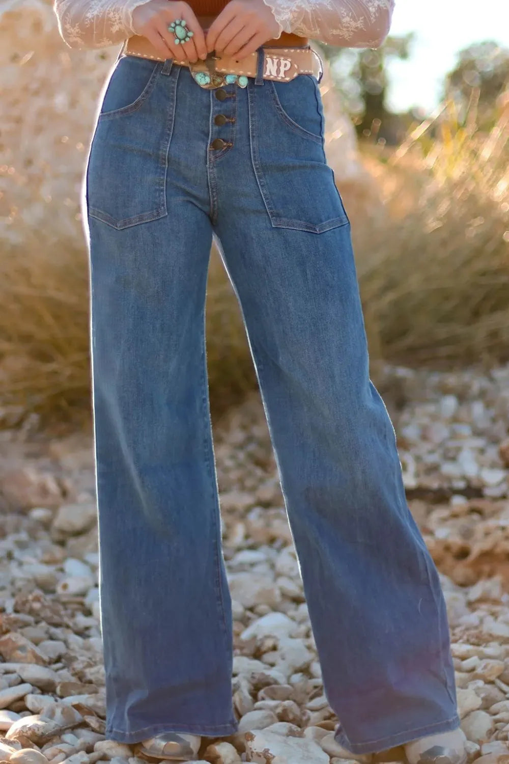 Person wearing blue bell-bottom jeans standing on a rocky surface with a blurred natural background