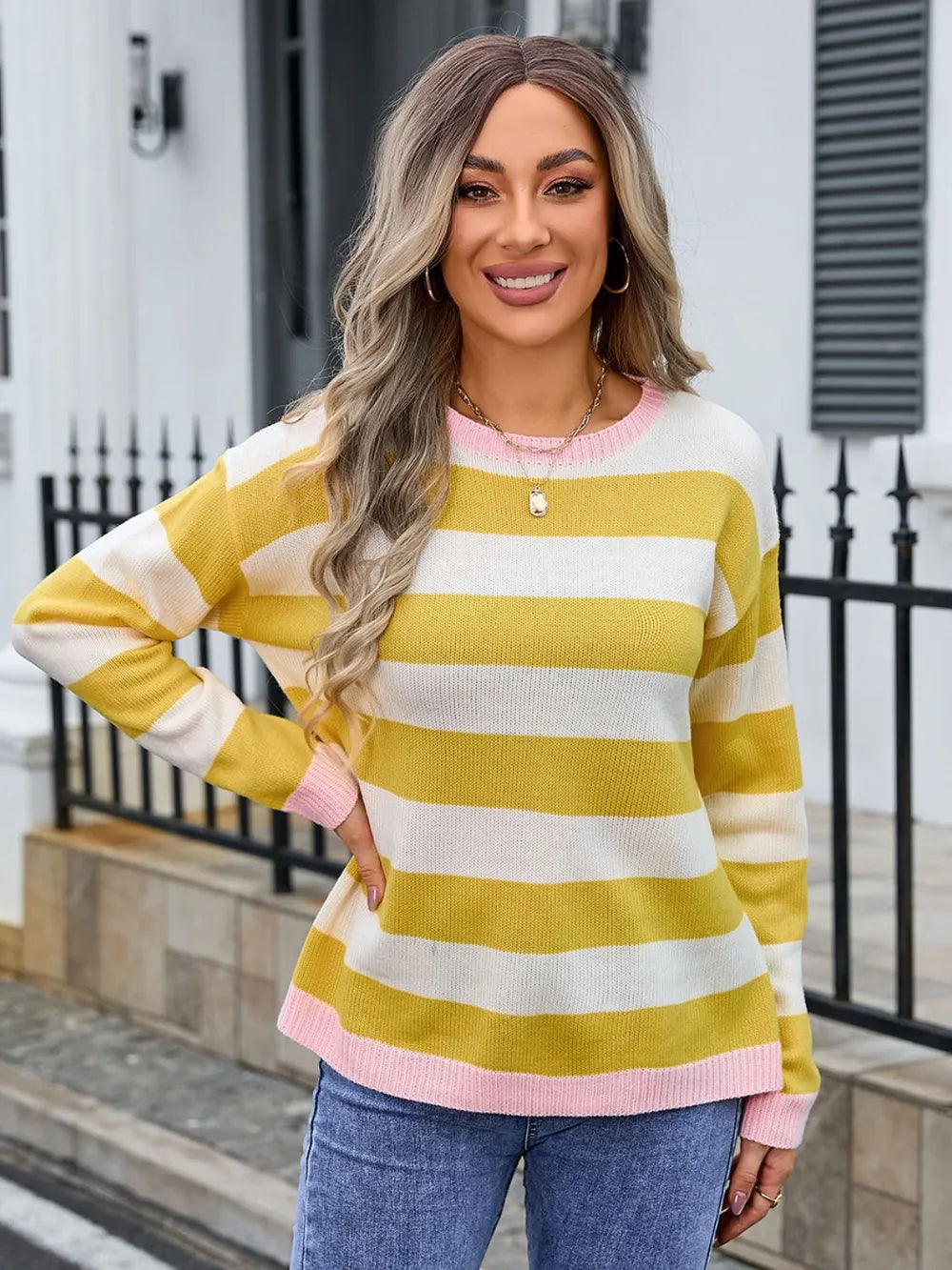 Woman wearing a yellow and white striped sweater with pink accents, standing on a sidewalk.