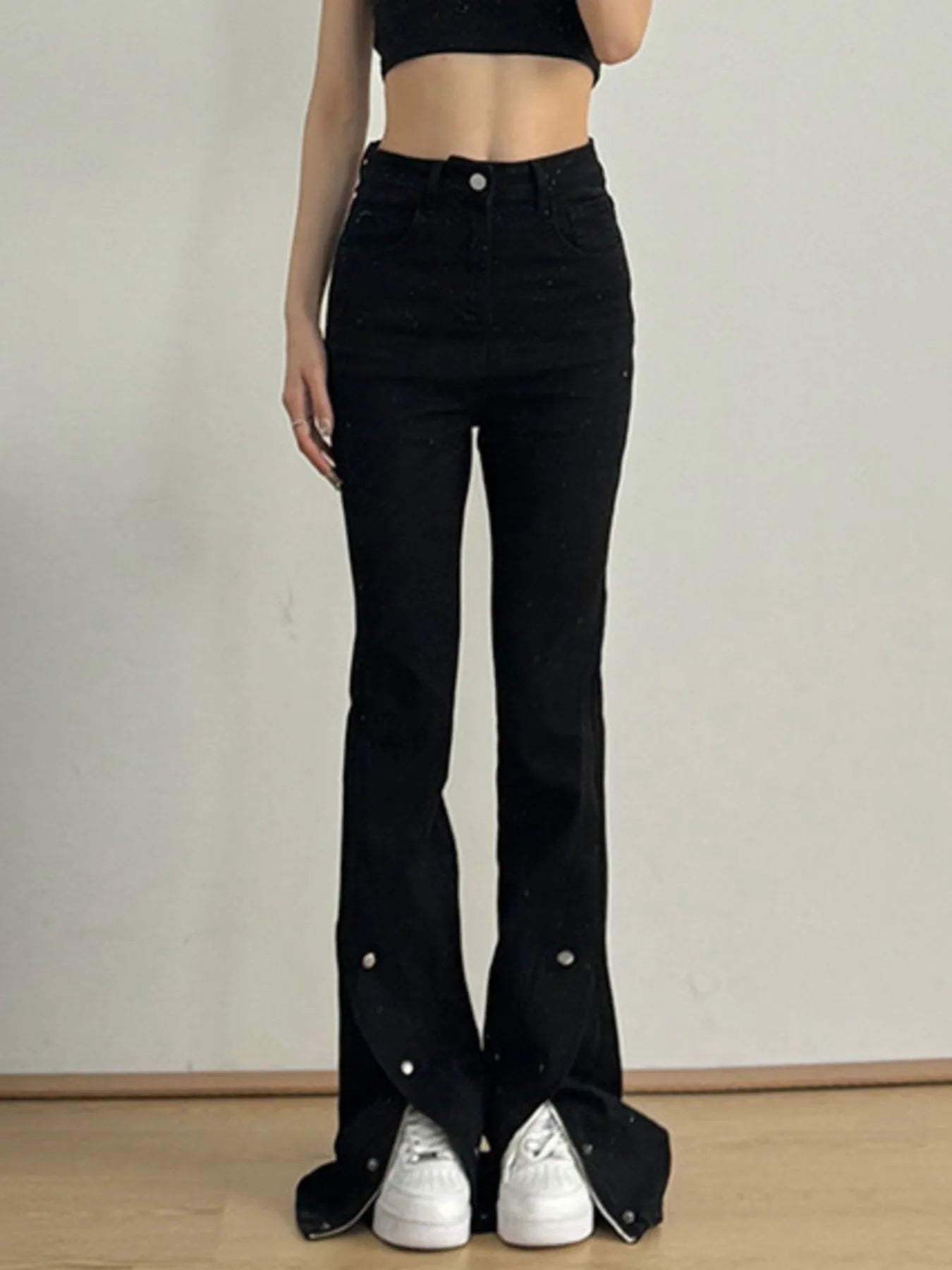 Person wearing black flared jeans with decorative buttons on a plain background