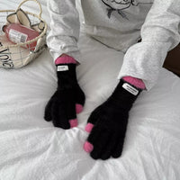 Person wearing black gloves with pink tips on a white surface