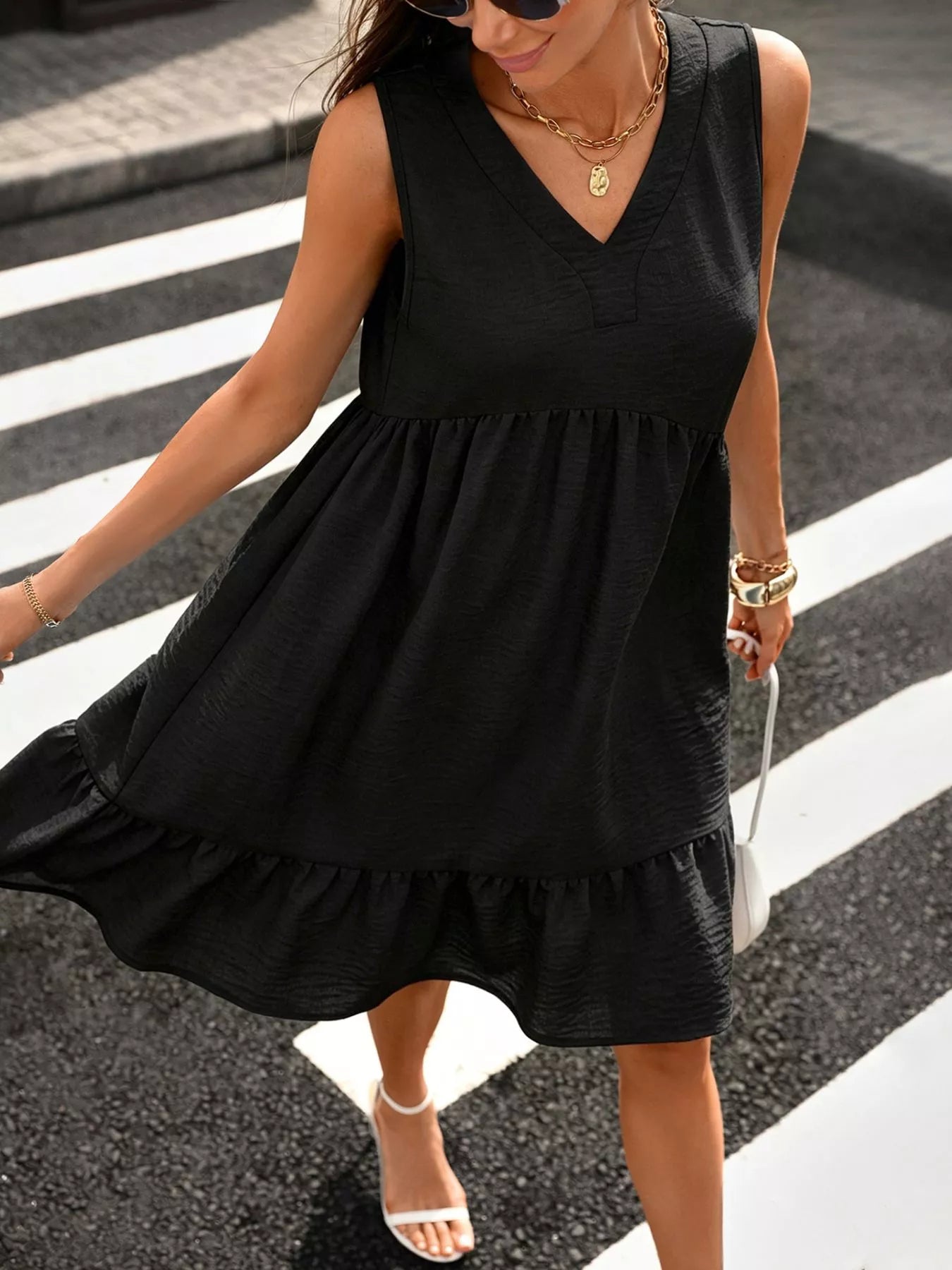 Woman wearing a black sleeveless dress crossing a street.