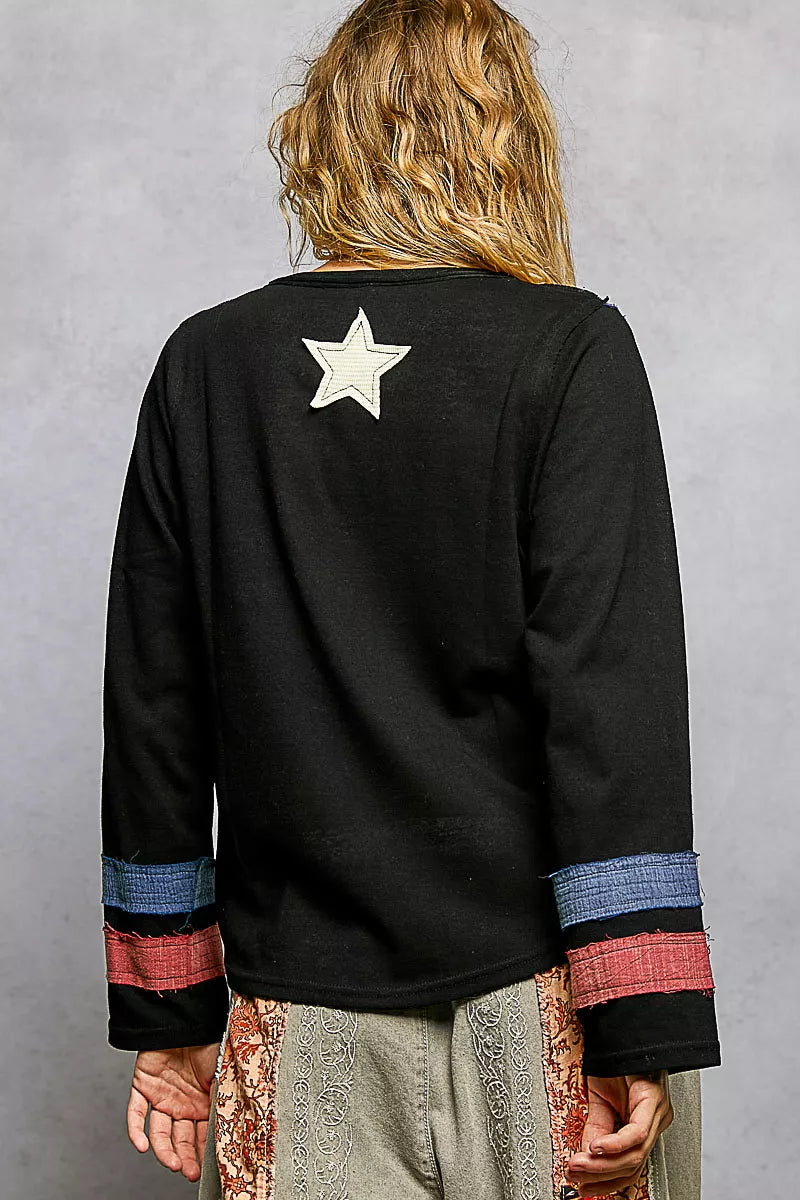 Black long-sleeve top with a star design on the back, worn by a person against a gray background.