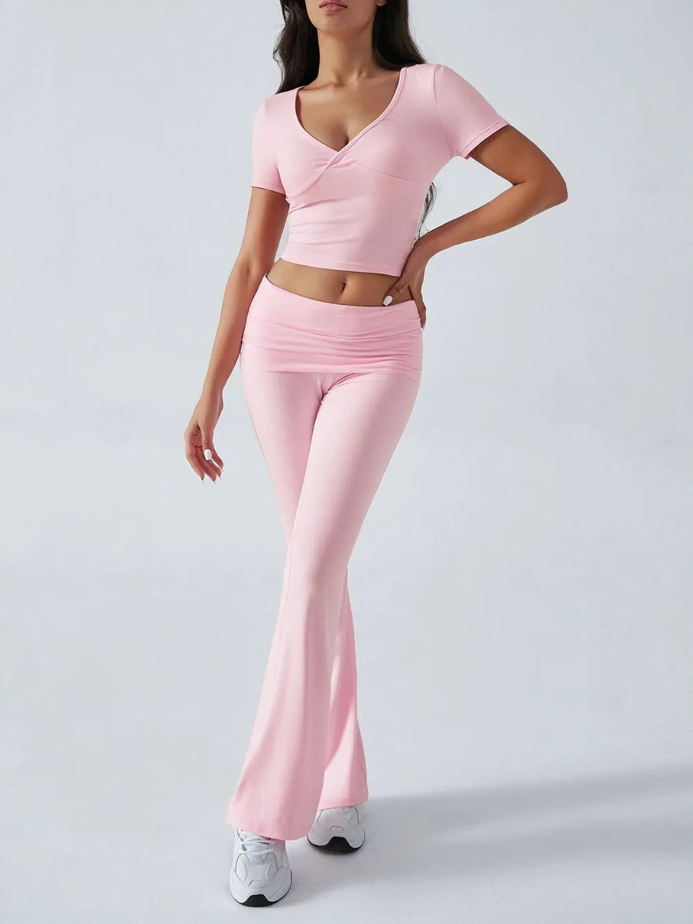 Person wearing a pink outfit with a top and flared pants on a white background