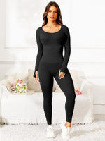 Woman wearing a black bodysuit standing in a room with a white couch and decorative pillows.