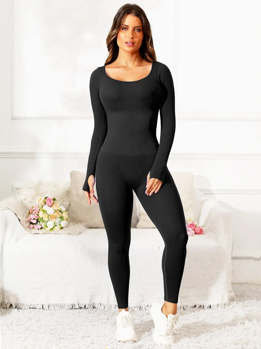 Woman wearing a black bodysuit standing in a room with a white couch and decorative pillows.