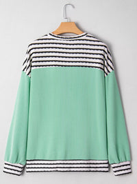 Green and black striped sweater on a hanger against a gray background