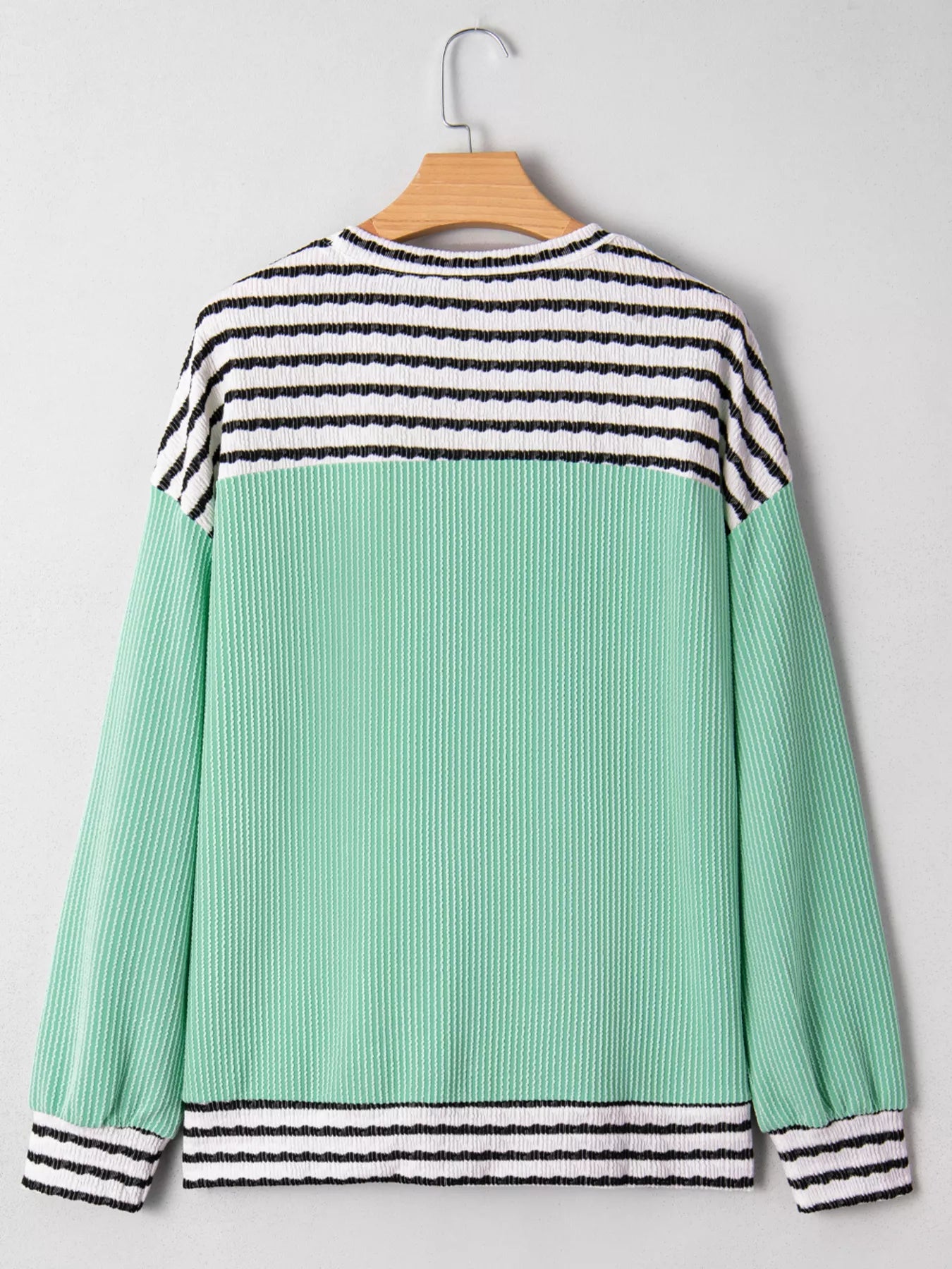 Green and black striped sweater on a hanger against a gray background