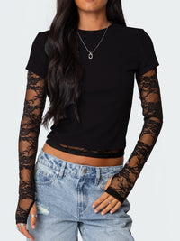 Person wearing a black long-sleeve top with lace sleeves and blue jeans on a white background