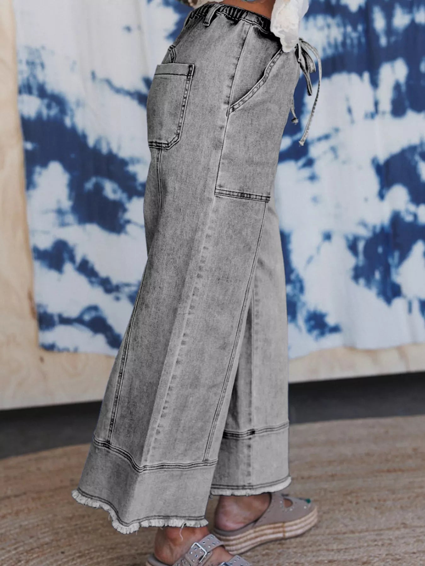 Gray wide-leg jeans worn by a person with a tie-dye wall in the background