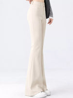 A model is shown from the waist down wearing high-waisted, wide-leg cream pants, a dark gray long-sleeve top, and white sneakers against a plain white studio background.