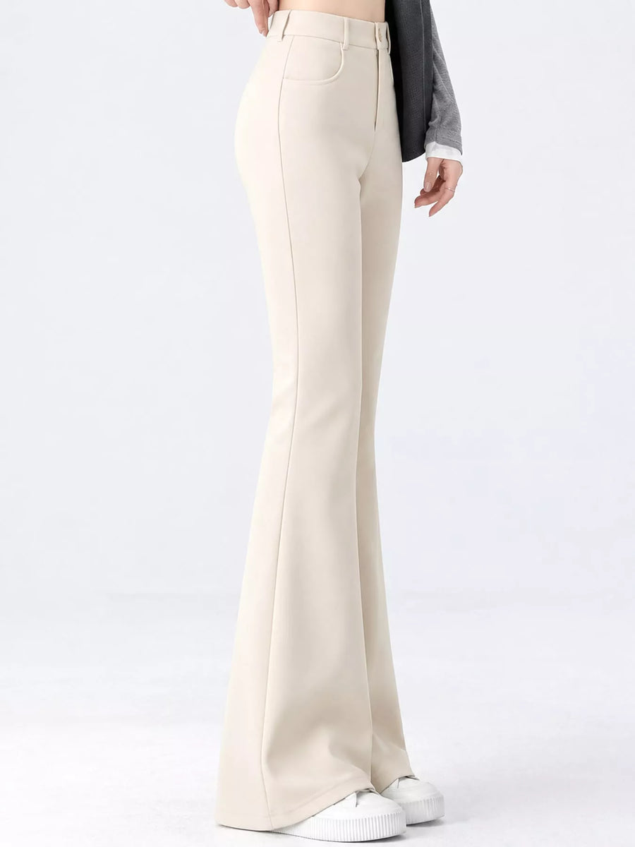 A model is shown from the waist down wearing high-waisted, wide-leg cream pants, a dark gray long-sleeve top, and white sneakers against a plain white studio background.