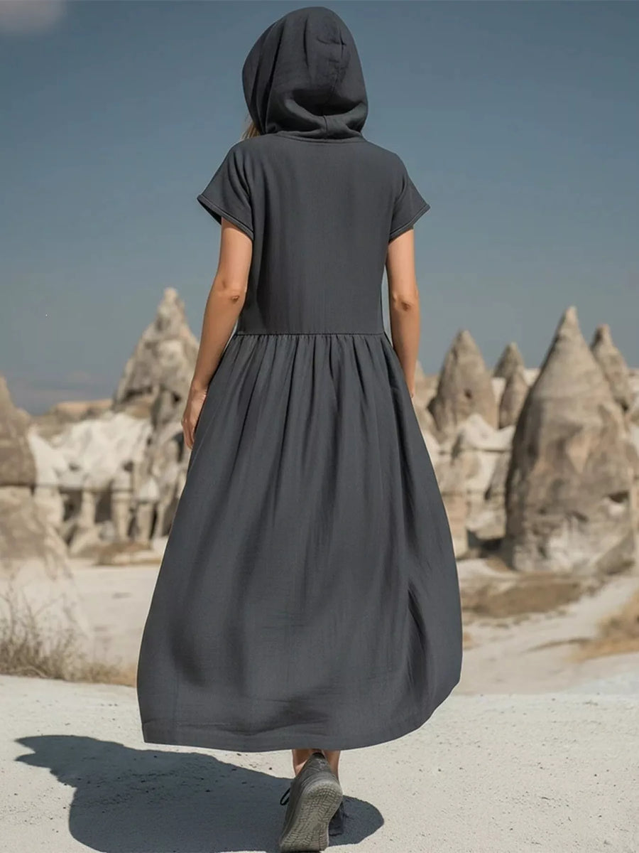 Person wearing a dark gray dress with a hood in a desert landscape with rock formations.