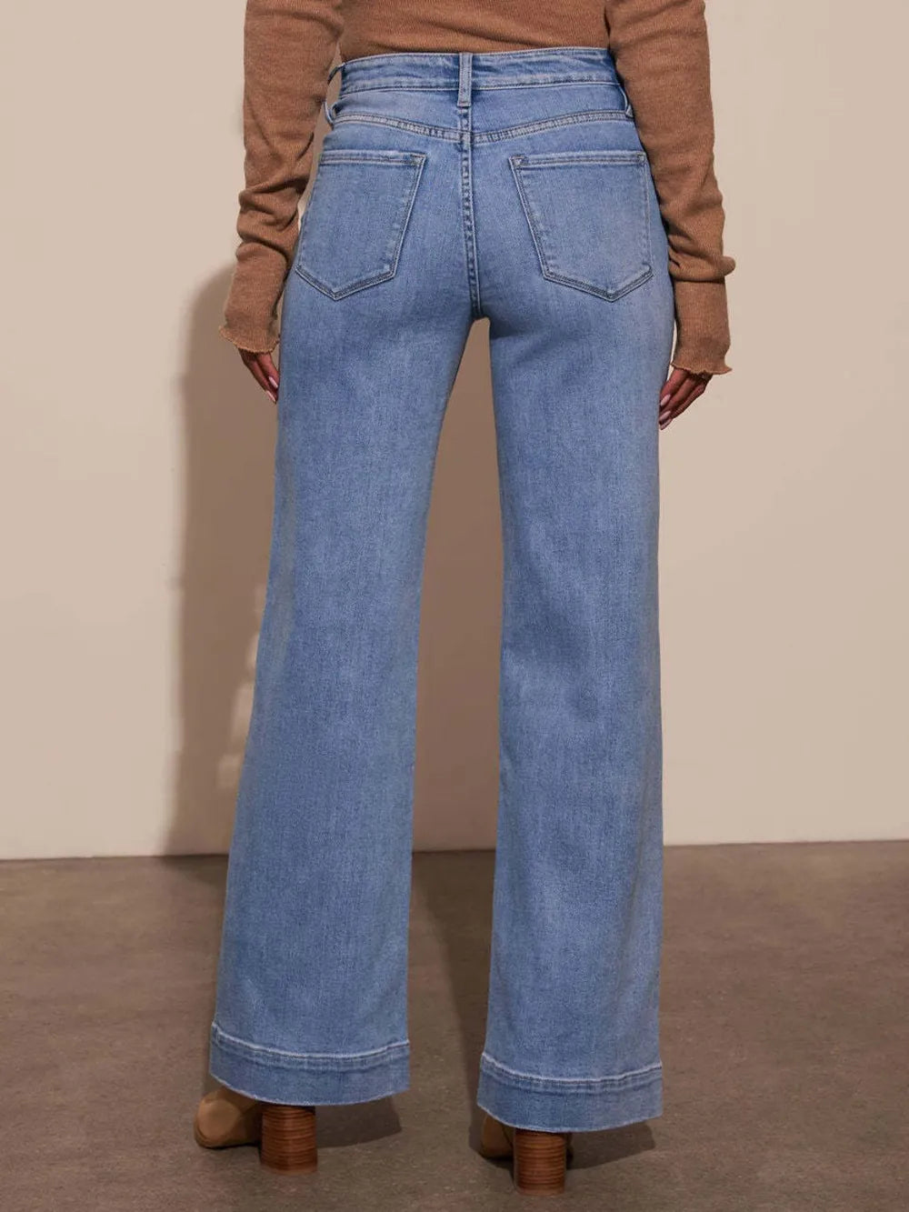Person wearing blue jeans and a brown sweater on a plain background