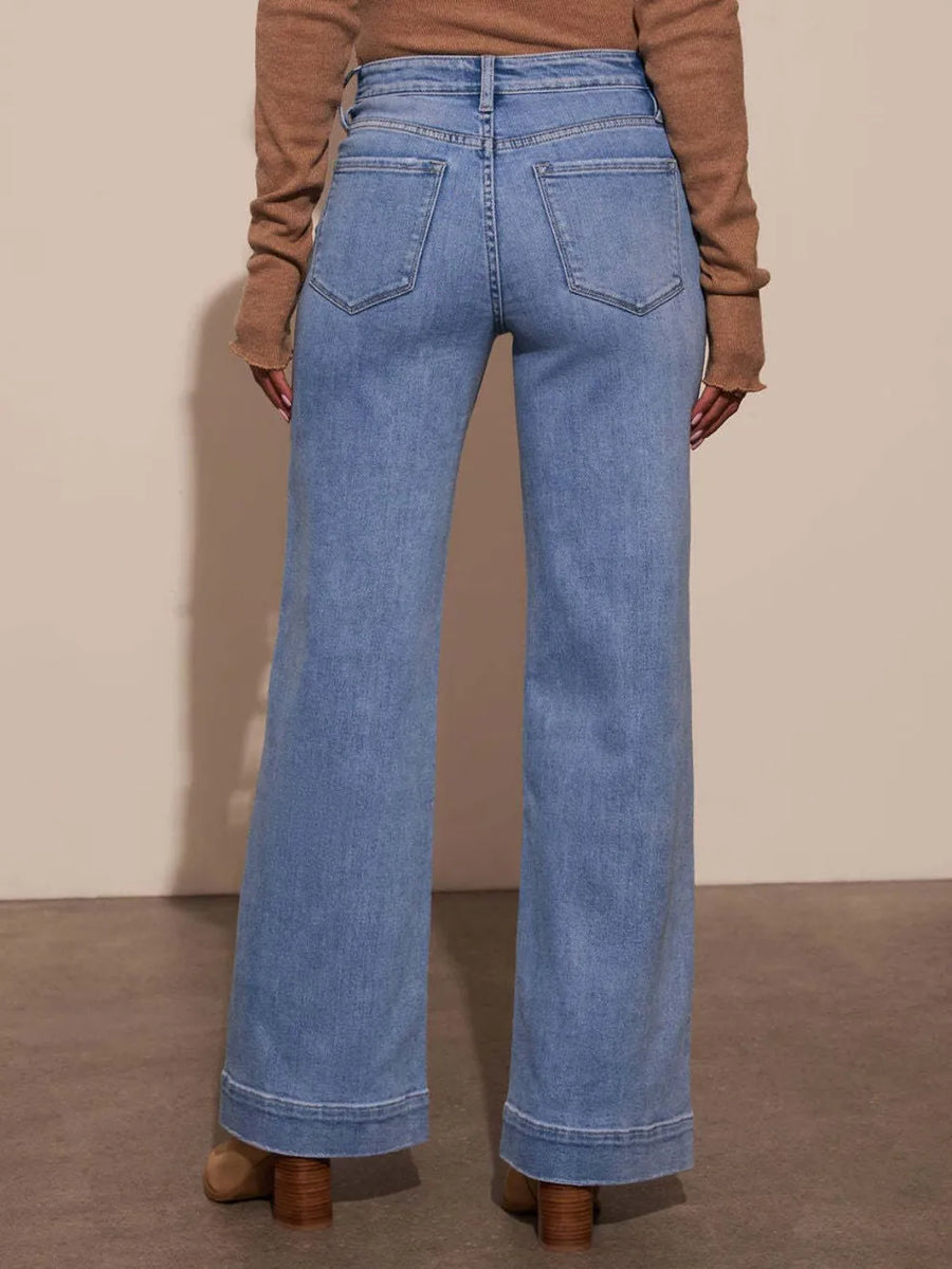 Person wearing blue jeans and a brown sweater on a plain background