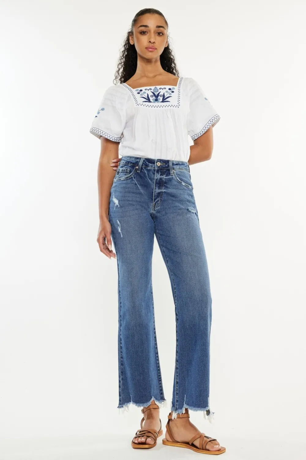 Woman wearing a white embroidered top and blue jeans on a white background