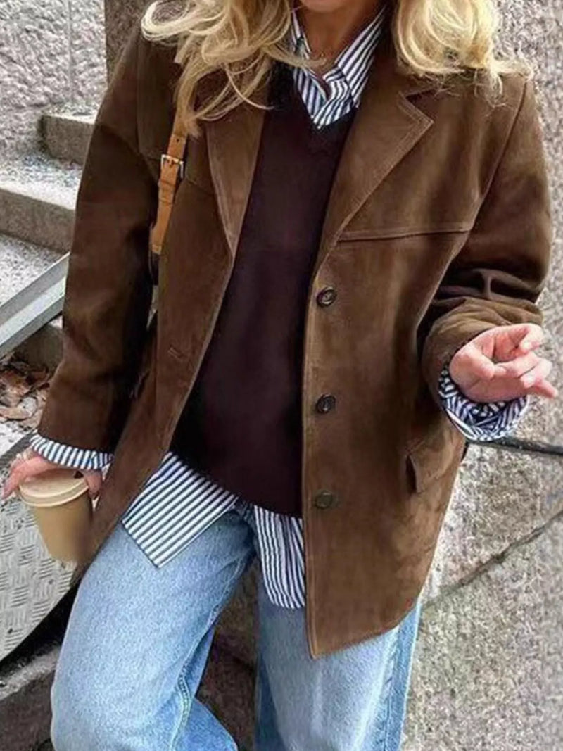 Person wearing a brown coat over a striped shirt with blue jeans, holding a coffee cup.