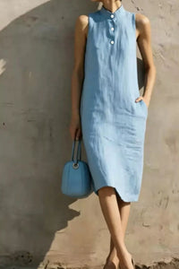 Woman wearing a light blue dress holding a matching handbag against a plain background