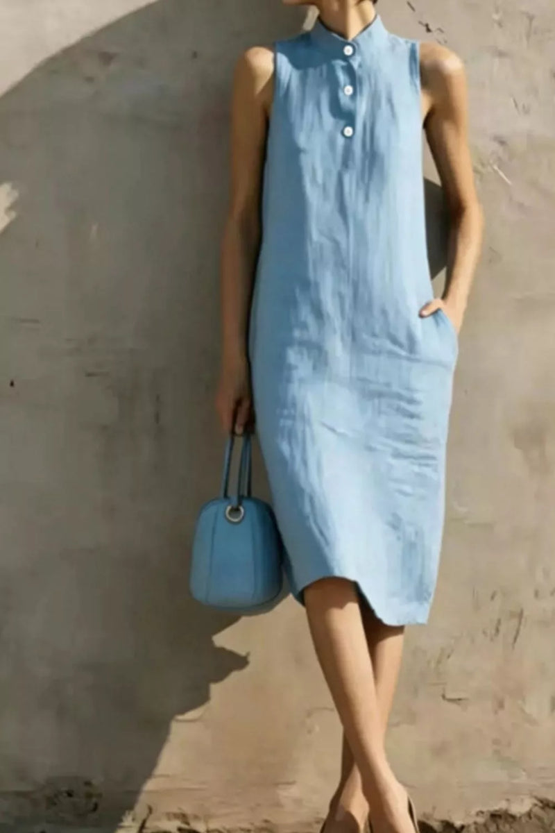 Woman wearing a light blue dress holding a matching handbag against a plain background