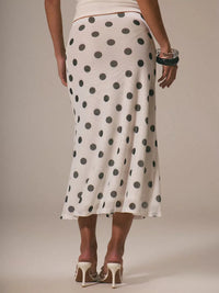 Person wearing a white skirt with black polka dots on a plain background