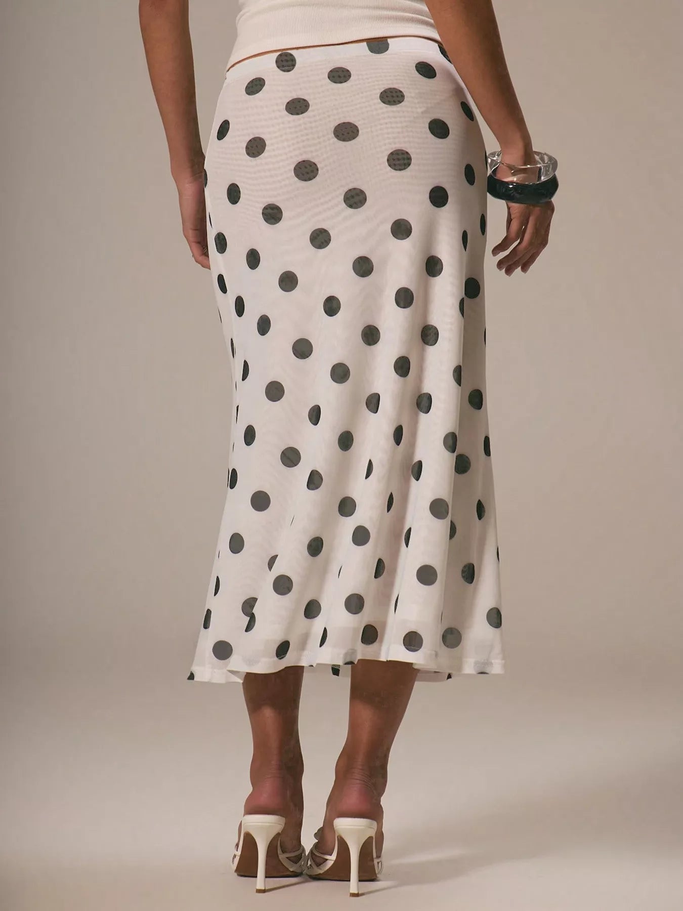 Person wearing a white skirt with black polka dots on a plain background