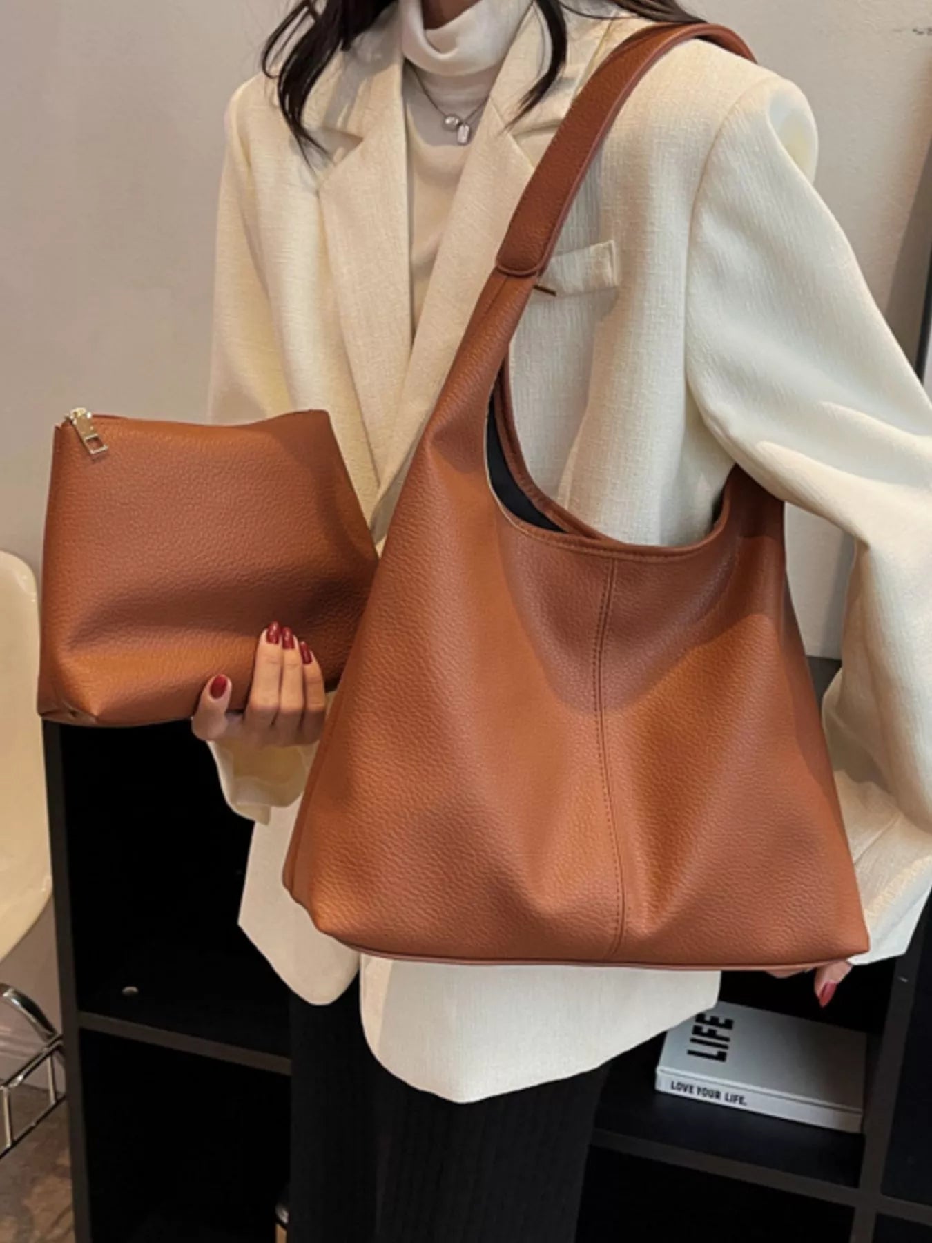 Person holding a brown leather handbag and clutch.