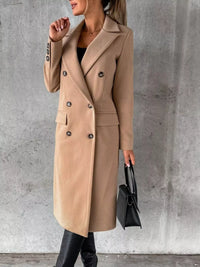 Person wearing a beige coat holding a black handbag against a gray concrete wall.