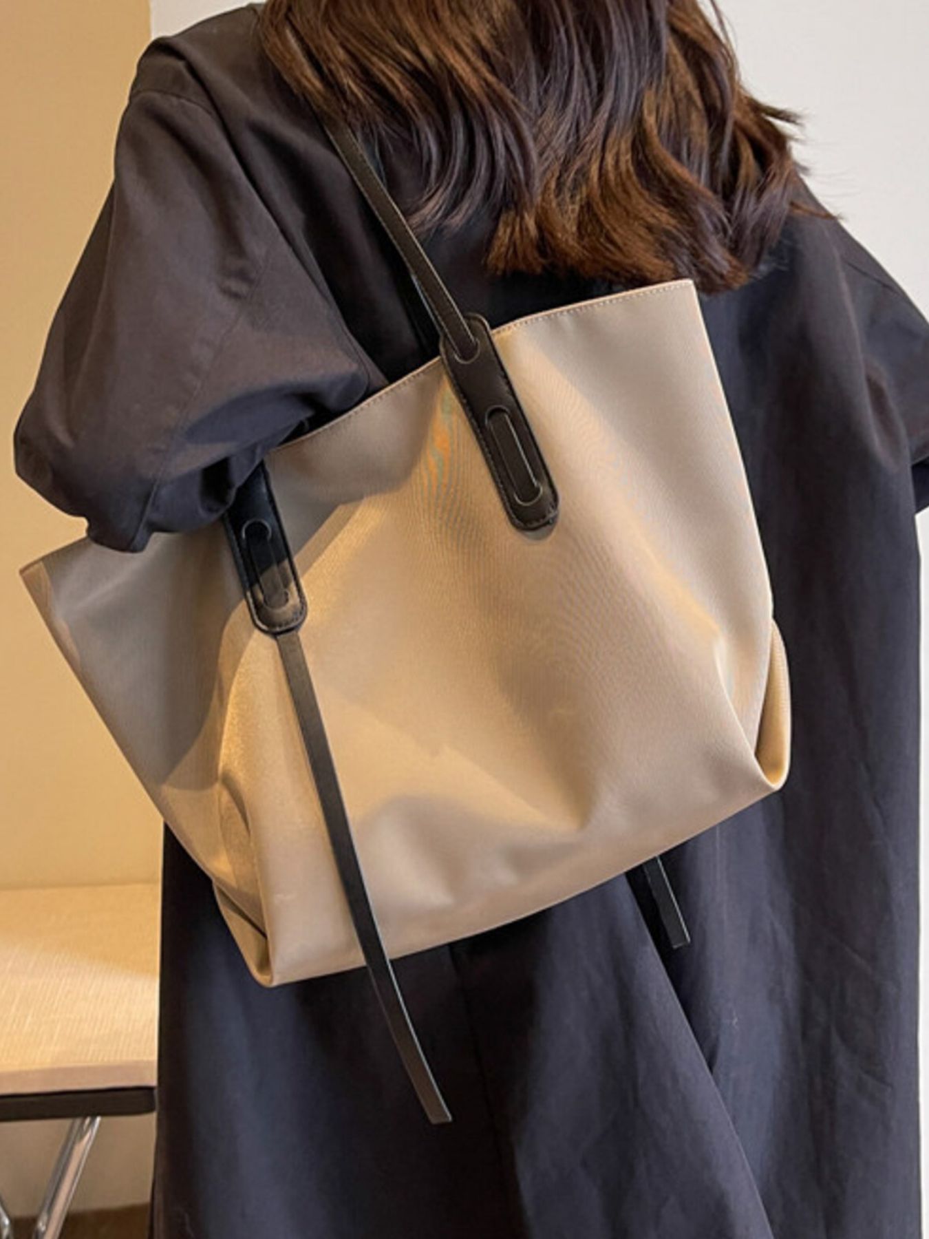 Person wearing a beige tote bag with black straps on a plain background