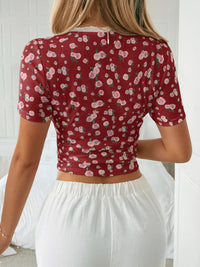 Person wearing a red floral crop top and white pants against a white background
