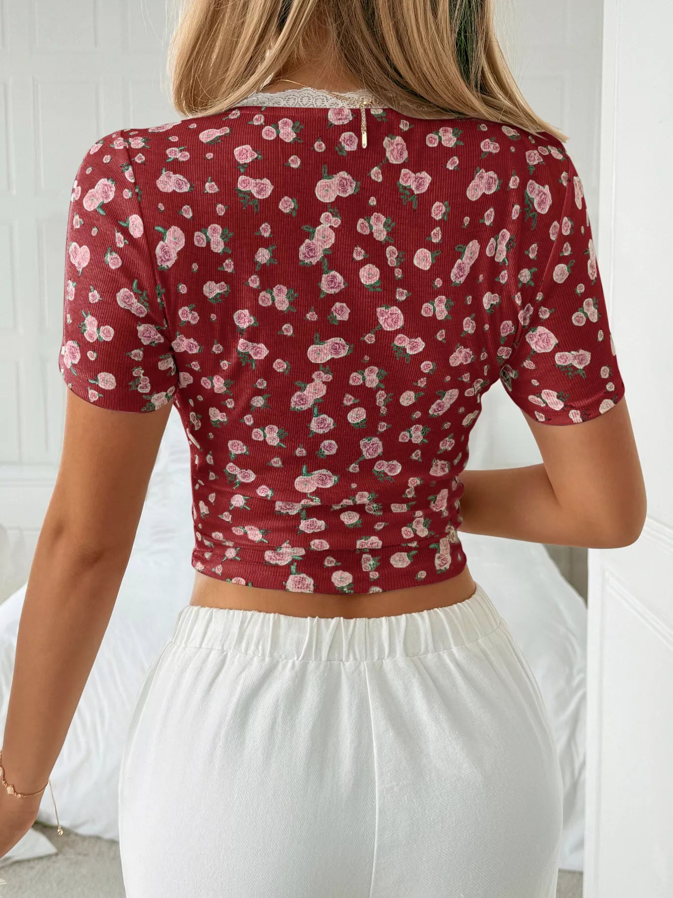 Person wearing a red floral crop top and white pants against a white background