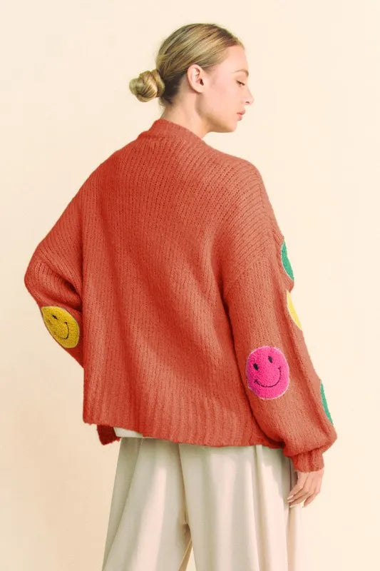 Person wearing a red sweater with smiley face patches on a beige background