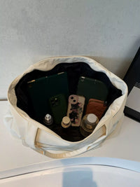 Open beige bag with electronic devices and small items on a light gray surface.