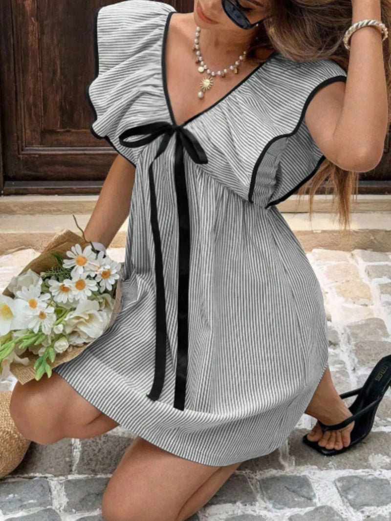 Woman wearing a black and white striped dress with a bow, standing on a stone path.
