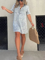 Woman wearing a light blue denim dress holding a woven bag against a plain background