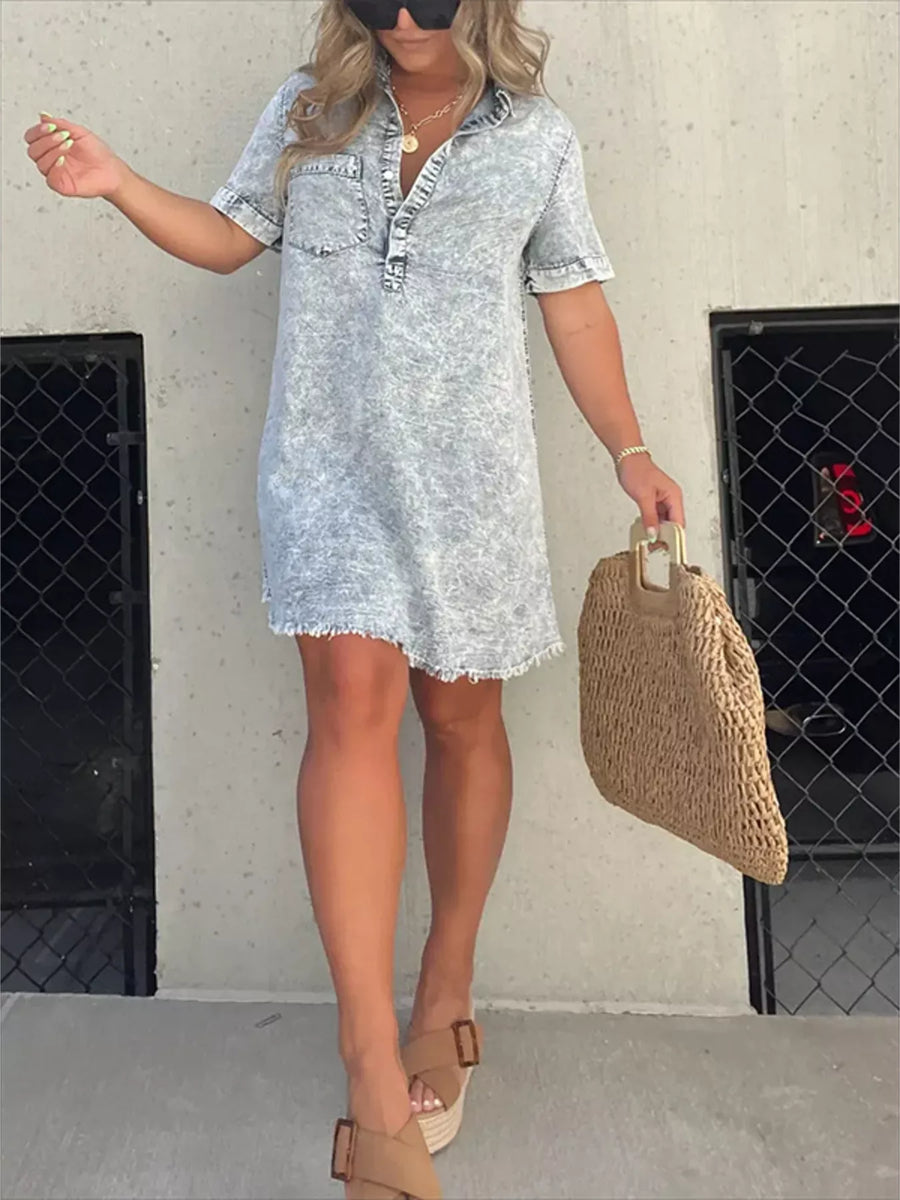 Woman wearing a light blue denim dress holding a woven bag against a plain background
