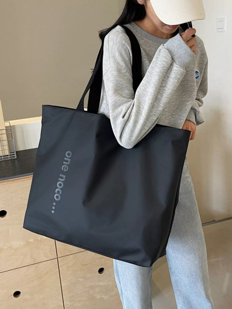 Person holding a black tote bag with 'one noco' branding indoors.