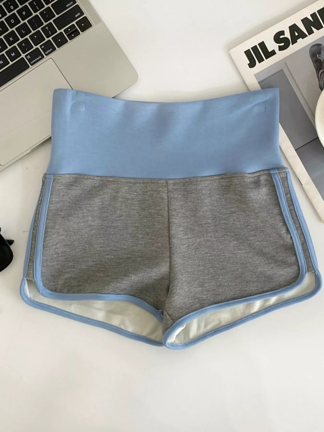 Gray shorts with blue trim on a white surface next to a laptop and magazine.