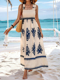 Woman in a long dress with blue patterns standing on a beach.