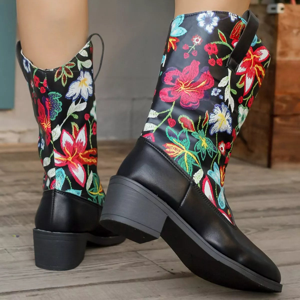 Black rain boots with colorful floral embroidery on a wooden floor.