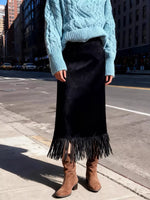 Person wearing a blue cable knit sweater, black fringed skirt, and brown boots on a city street.