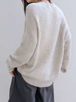 Person wearing a light gray sweater and dark pants against a plain background