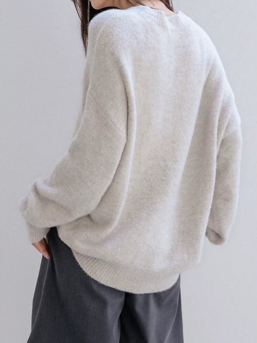 Person wearing a light gray sweater and dark pants against a plain background