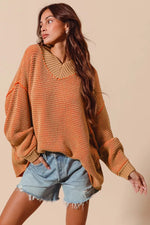 Woman wearing a brown oversized sweater and denim shorts against a beige background