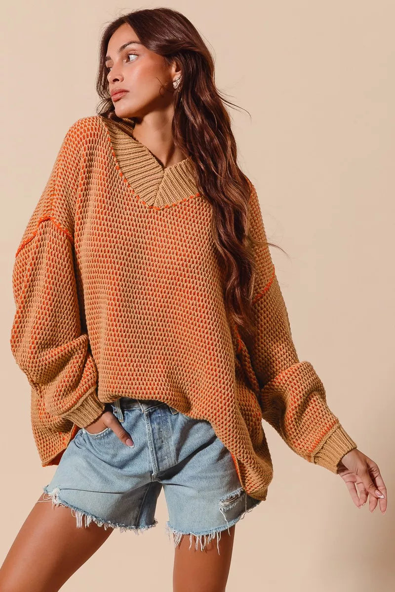 Woman wearing a brown oversized sweater and denim shorts against a beige background
