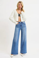 Woman wearing a white jacket, black top, and blue jeans on a white background