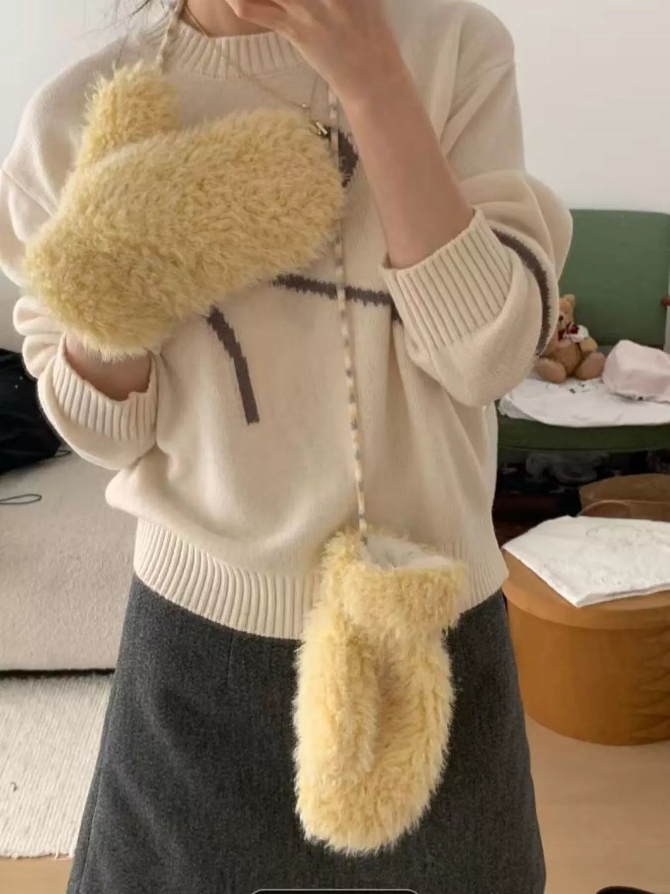 Person wearing a cream sweater and dark skirt with fluffy yellow gloves.