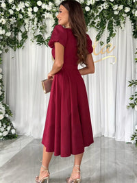 Woman in a burgundy dress standing in front of floral decorations.